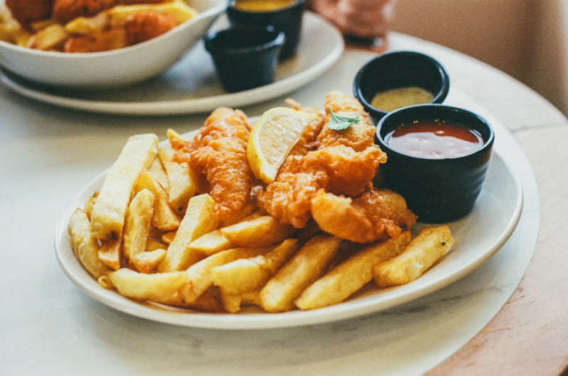Plato de fish and chips con pescado rebozado crujiente, patatas fritas y salsas, una comida tradicional británica.