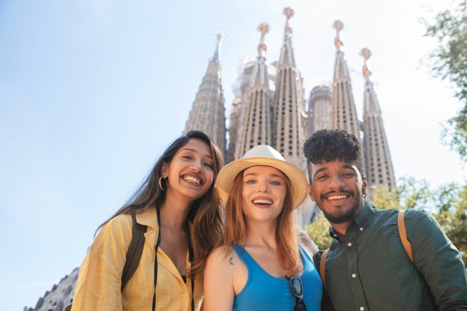 Dos chicas y un chico sonríen frente a la majestuosa Sagrada Familia en Barcelona, disfrutando de un día soleado mientras exploran la ciudad.