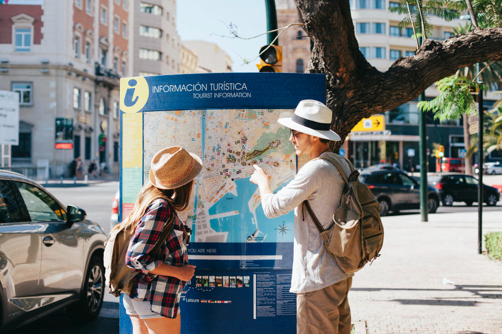 Chico y chica junto a un punto de información turística durante un viaje.