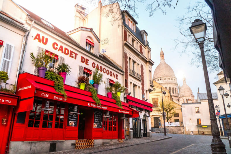Cafetería y restaurante tradicional en el barrio de Montmartre, París, con la basílica del Sagrado Corazón visible al fondo.