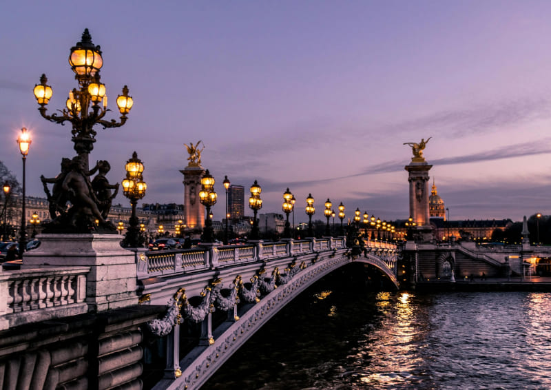 Puente Alejandro III iluminado al atardecer sobre el río Sena en París, con sus elegantes farolas y detalles ornamentales.