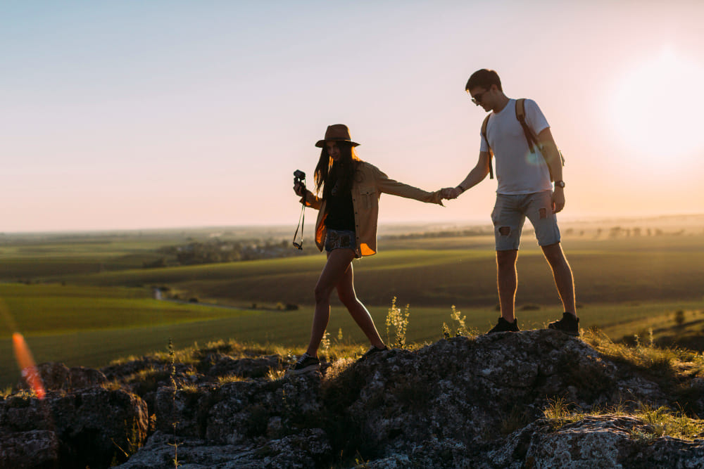 Pareja haciendo senderismo y caminando de la mano sobre rocas al atardecer en un entorno natural.